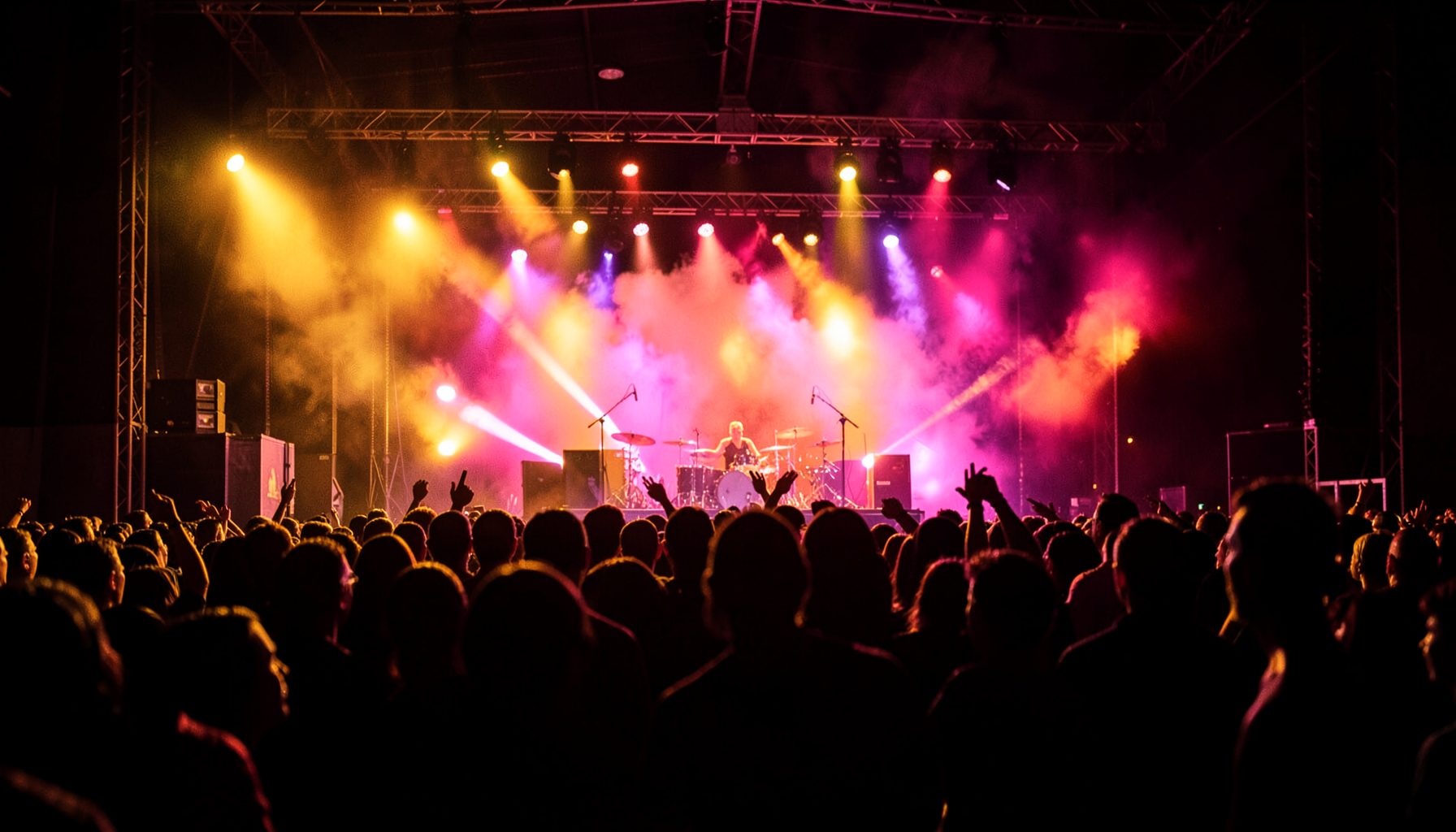 Vibrant concert-stage scene with warm amber and magenta stage lights, silhouetted crowd in the foreground