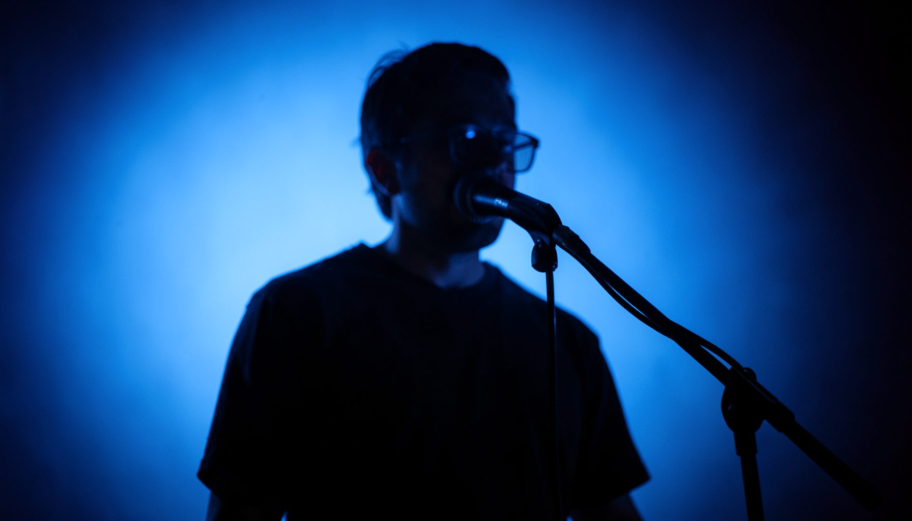 Moody studio performance with soft blue backlighting and a single microphone on a stand